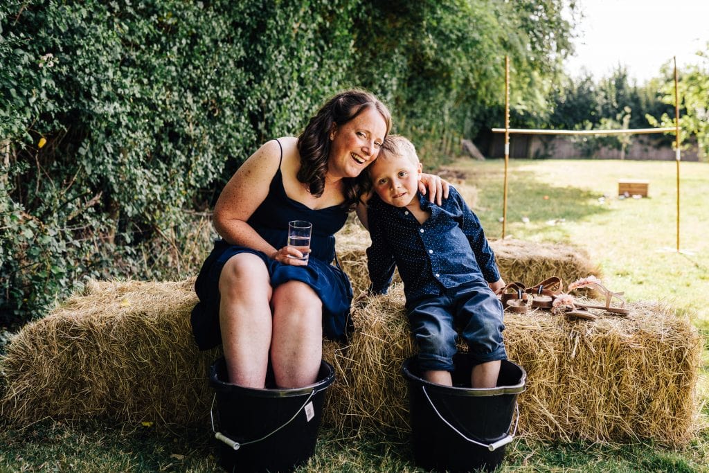 A mum and her son cool themselves down at this Cotswold summer wedding by dipping their feet in buckets of cold water.