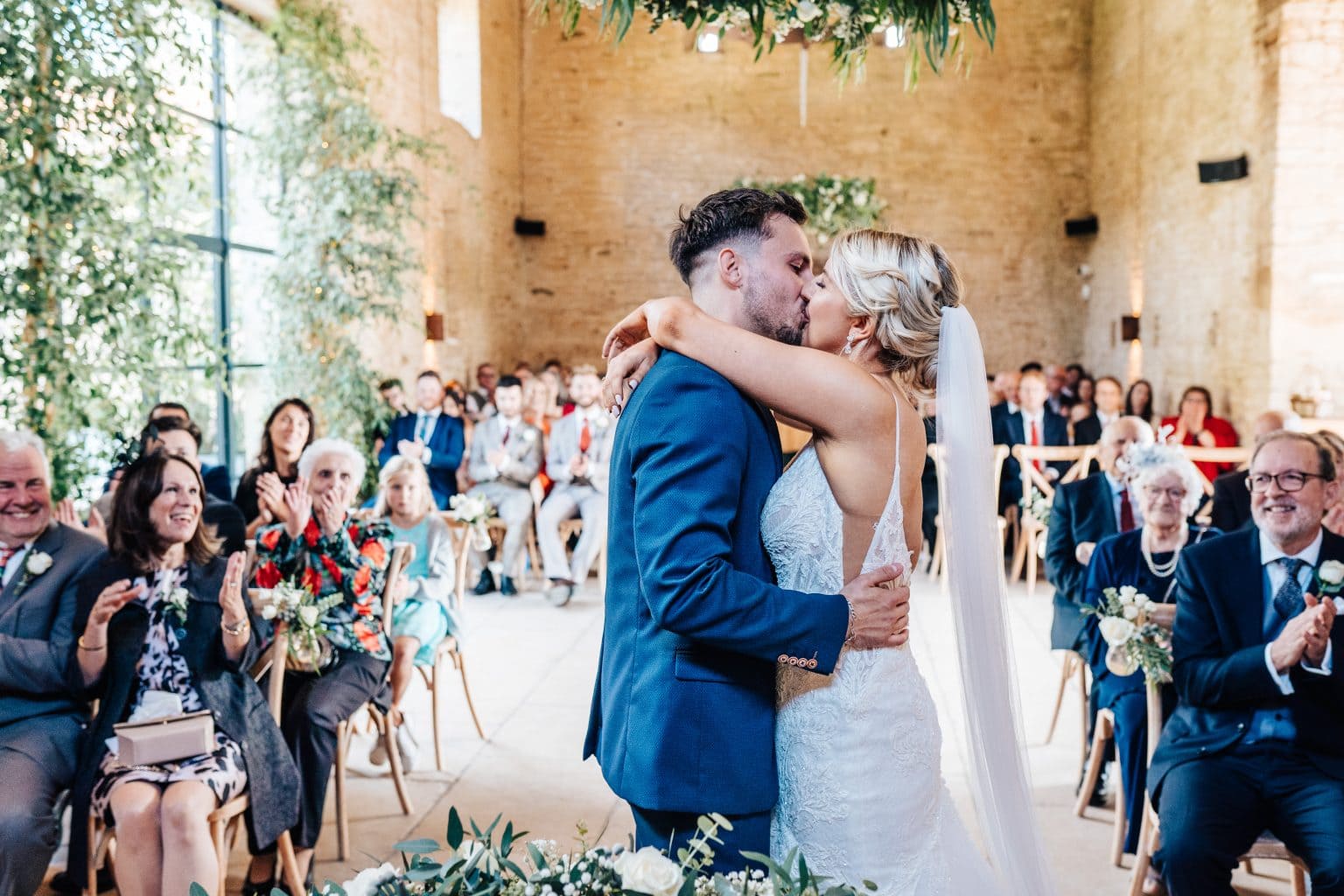 "Just married" and a "you may kiss the bride" as couple embrace for their first kiss as a married couple at Old Gore Barn by Yard Space In Cirencester