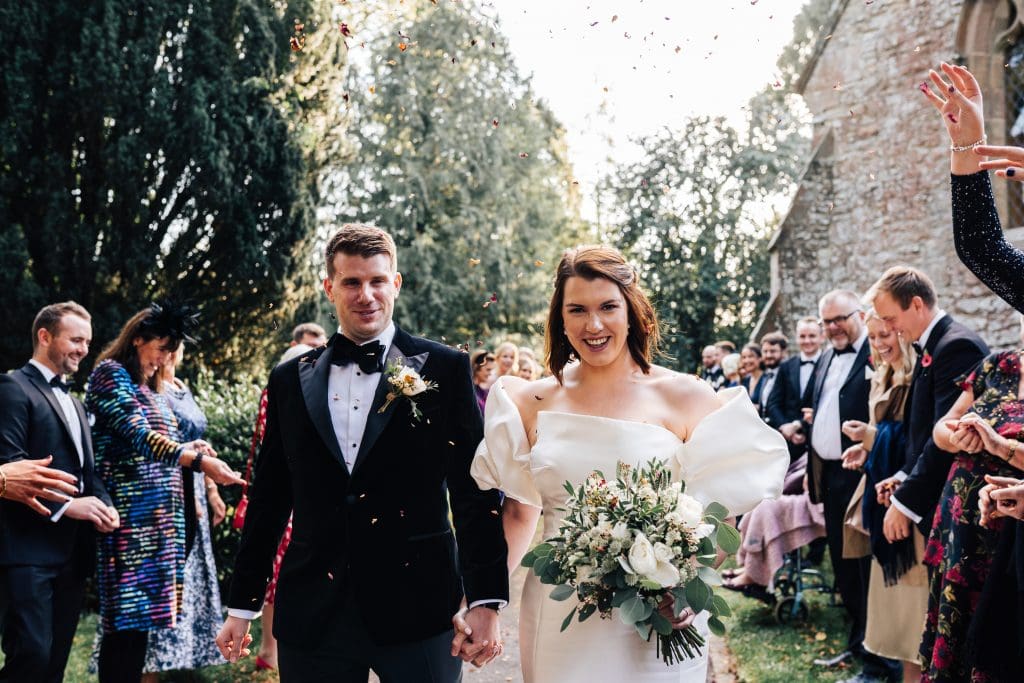 Sun shines through on Andrew and Sarah as they walk through a sea of confetti at Birtsmorton Court.