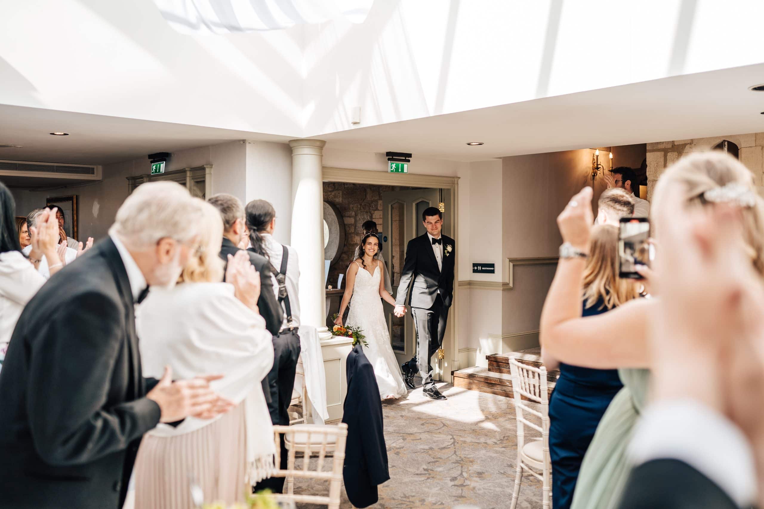 Wedding party at Ellenborough Park Hotel applaud the bride and groom as they enter their wedding reception