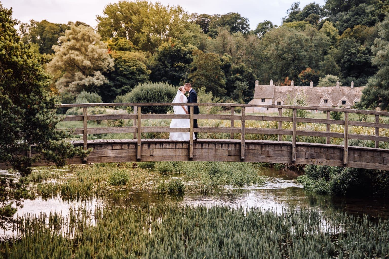 Summer wedding at The Swan Hotel in Bibury with Laura and Phil kissing on the bridge, overlooking the gorgeous Bibury landscape.