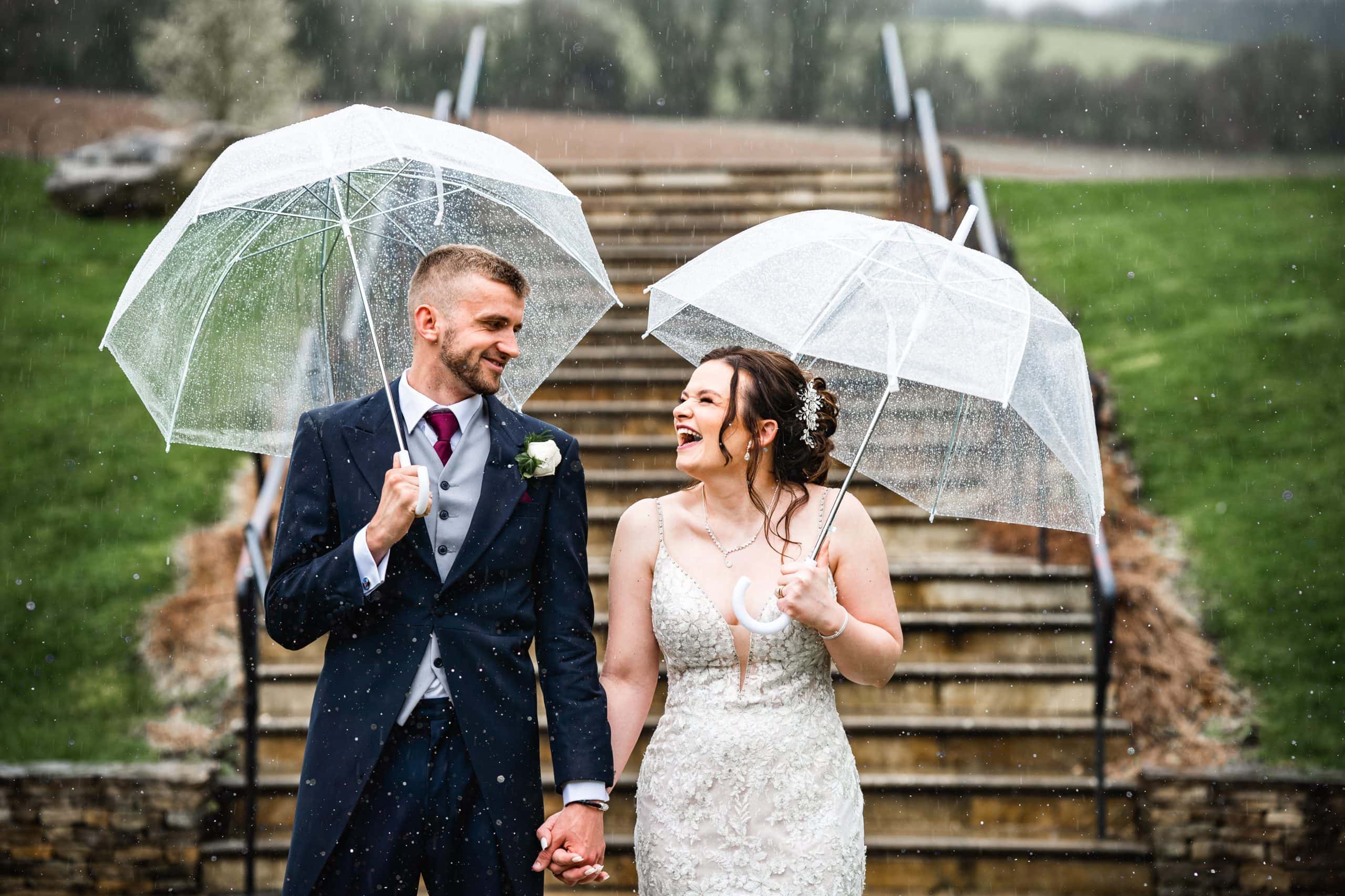 It may be raining but this couple won't stop smiling whilst celebrating their wedding day, under an umbrella, at The Barn at Upcote, Cheltenham