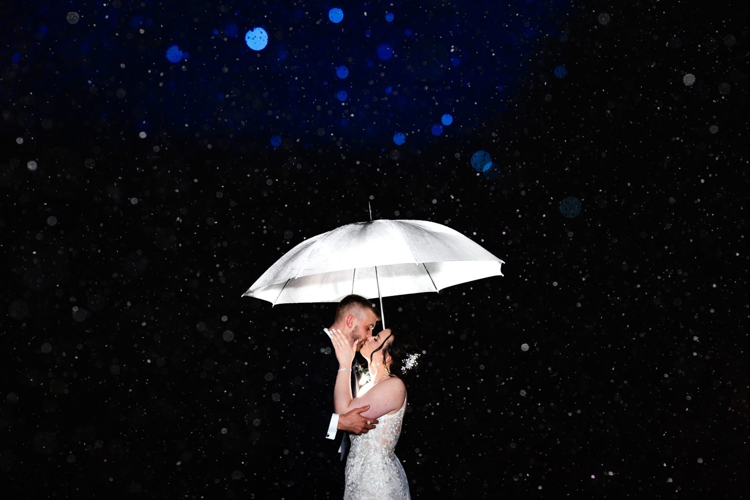 Rain hammers down in the dark but the scene is beautifully lit up by photographer Pedge Photography to deliver this stunning, in the dark photo of Mollie & Matt kissing under at The Barn at Upcote, Cheltenham